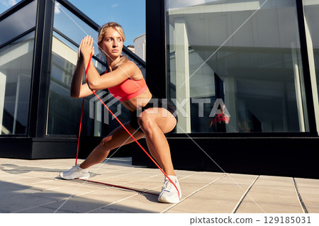 Woman performing resistance band exercise outdoors near a modern glass building Woman performing resistance band exercise outdoors near a modern glass building 129185031