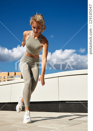 Fit woman exercising outdoors on a sunny day against a blue sky Fit woman exercising outdoors on a sunny day against a blue sky 129185047