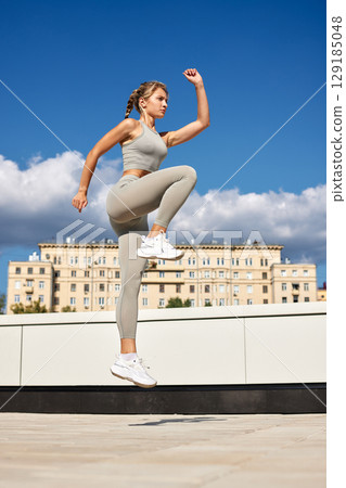 Young woman performing a fitness jump exercise outdoors in daytime 129185048