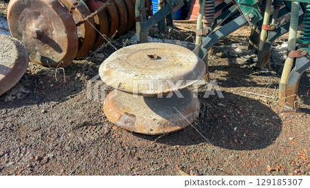 Close-up of old, rusty agricultural disc blades on soil, part of a vintage farm machine, symbolizing forgotten labor or rural history. 129185307