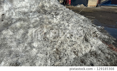 Large pile of dirty, melting snow in an urban or industrial area. 129185308