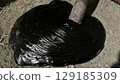 Thick black viscous liquid, resembling crude oil or tar, flowing from a metal pipe onto dry ground, symbolizing industrial waste or pollution. 129185309