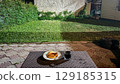 Night snack on outdoor table in backyard garden. A plate with baked pastries and a glass of dark soda on a wicker-style table in a backyard at night. The yard is lit with artificial light. 129185315