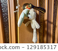 Two small plush toys, a puppy and a bear, hanging from a door handle inside a cozy room. Warm, nostalgic atmosphere. 129185317