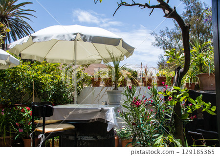 White umbrellas and tables on a restaurant terrace under bright sunlight in Betancuria, Fuerteventura White umbrellas and tables on a restaurant terrace under bright sunlight in Betancuria, Fuerteventura 129185365