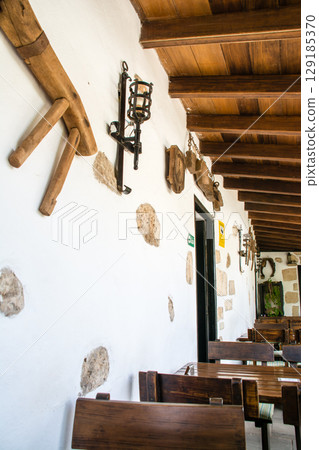 A bright restaurant with white walls and wooden tables and chairs next to the terrace in Betancuria, Fuerteventura A bright restaurant with white walls and wooden tables and chairs next to the terrace in Betancuria, Fuerteventura 129185370
