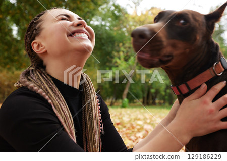Joyful woman with her playful dog in a sunny autumn park 129186229