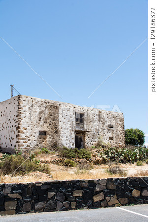 An abandoned house with white walls and rocks built into it in bright sunlight in Betancuria, Fuerteventura 129186372