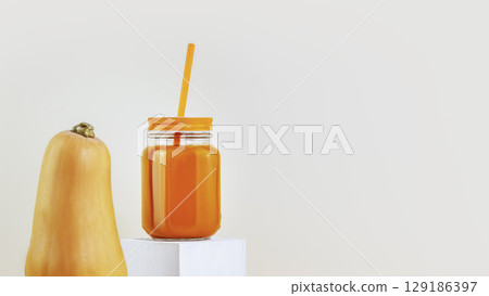 Pumpkin juice. Pumpkin with glass with a straw of natural pumpkin juice on a light background with copy space. Vegan or vegetarian diet. Natural healthy drink. Organic vegetable juice Pumpkin juice. Pumpkin with glass with a straw of natural pumpkin juice on a light background with copy space. Vegan or vegetarian diet. Natural healthy drink. Organic vegetable juice 129186397