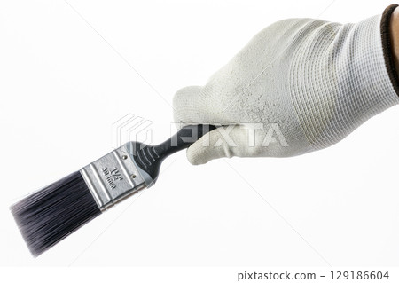 Hand wearing white rubber glove holds paintbrush with black handle against white background, suggesting focus on painting or DIY activities 129186604
