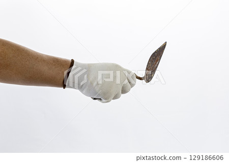 Hand wearing white rubber glove holds rusty trowel against plain background, suggesting focus on gardening or construction work 129186606