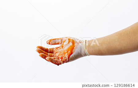 Hand wearing rubber glove is covered in red liquid, resembling blood, against white background. image evokes sense of urgency and caution 129186614