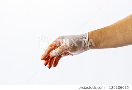 Gloved hand covered in red liquid, possibly blood, is extended against white background, suggesting medical or forensic context 129186615