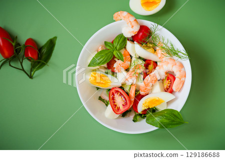 Diet dish with shrimps, tomatoes and boiled eggs on a green background 129186688