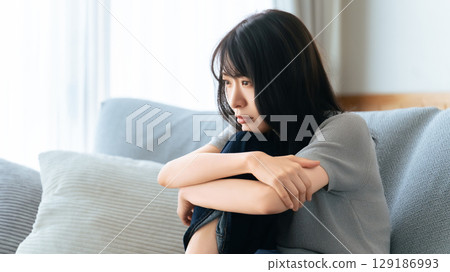 Woman sitting on the sofa in the living room thinking 129186993