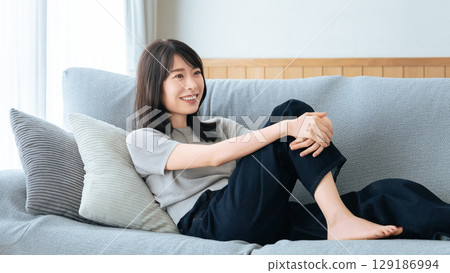 Smiling woman sitting on sofa in living room 129186994