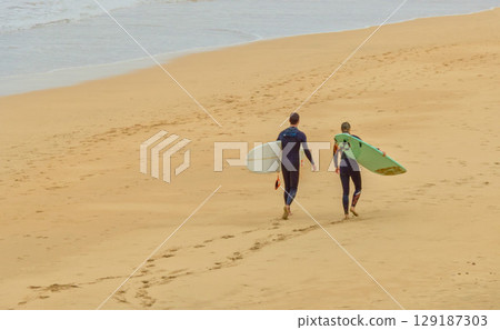 surfers strolling along the beach surfers strolling along the beach 129187303