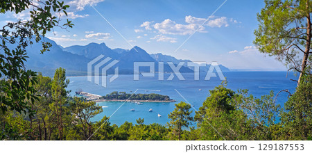 Panoramic Kemer coastal landscape. Vibrant seaside panorama with majestic Taurus mountains behind. Top view to the Moonlight beach and peninsula with a bustling harbor. Summertime holiday in Turkey Panoramic Kemer coastal landscape. Vibrant seaside panorama with majestic Taurus mountains behind. Top view to the Moonlight beach and peninsula with a bustling harbor. Summertime holiday in Turkey 129187553