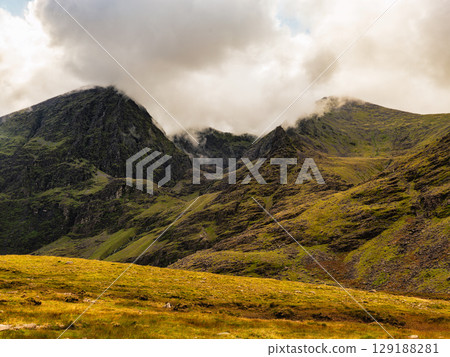 Lush green hillsides and mountainous terrain are seen at Carrauntoohil in County Kerry, Ireland. Cloudy skies create an awe-inspiring landscape at the highest peak in Ireland. Lush green hillsides and mountainous terrain are seen at Carrauntoohil in County Kerry, Ireland. Cloudy skies create an awe-inspiring landscape at the highest peak in Ireland. 129188281