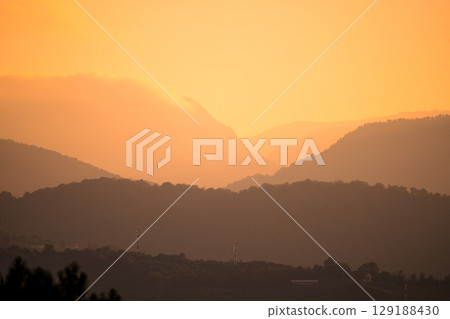 Sunrise over misty mountain layers creates a peaceful, atmospheric landscape in warm morning light. 129188430