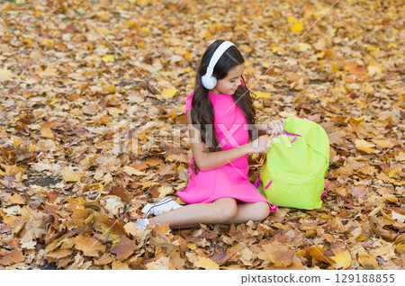 Time to relax. small girl wear headphones. back to school. modern education. child with school backpack in fall forest. concept of knowledge day. kid in autumn park. happy kid relax on autumn leaves Time to relax. small girl wear headphones. back to school. modern education. child with school backpack in fall forest. concept of knowledge day. kid in autumn park. happy kid relax on autumn leaves 129188855