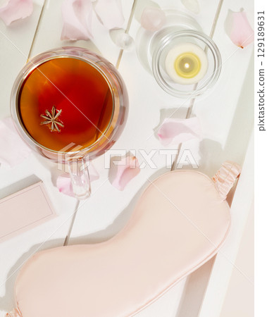 Sleep care composition with mask for sleep, cup of tea, candle and rose petals on a white wooden tray. Insomnia or depression treatment for sleepless nights. Concept of relax, self care and me time 129189631