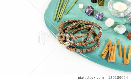 Self-care, healing composition with rosary beads, aroma sticks, chakra stones, sandalwood sticks and candle on a green marble podium with copy space. Concept of relax, energy healing and meditation 129189634