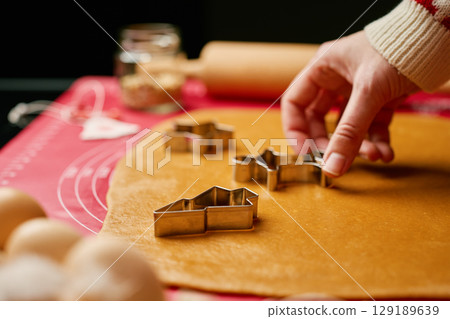 Close-up of hands pressing metal cookie cutter into gingerbread dough on silicone baking mat. Festive baking preparation and family traditions concept Close-up of hands pressing metal cookie cutter into gingerbread dough on silicone baking mat. Festive baking preparation and family traditions concept 129189639