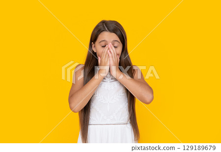 sneezing teen girl in white dress has long hair on yellow background 129189679