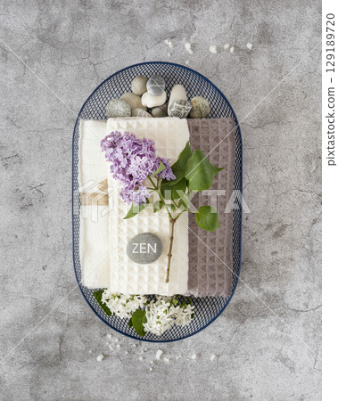 Wellness, Spa relax still life with massage stones with inscription Zen, towels and lilac flowers in a blue basket on a grey textured background. Self care and me time concept 129189720