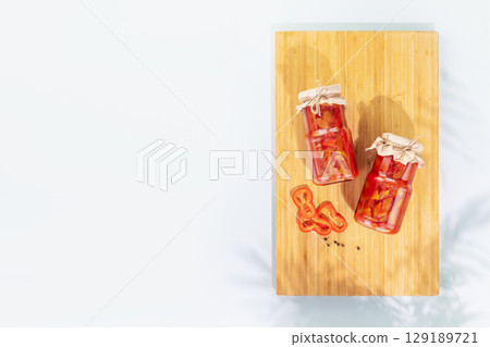 Probiotic food. Pickled or fermented vegetables. Lecho, sweet peppers in glass jars on a wooden board on a blue background with shadows and copy space. Mockup of food preserving or canning Probiotic food. Pickled or fermented vegetables. Lecho, sweet peppers in glass jars on a wooden board on a blue background with shadows and copy space. Mockup of food preserving or canning 129189721
