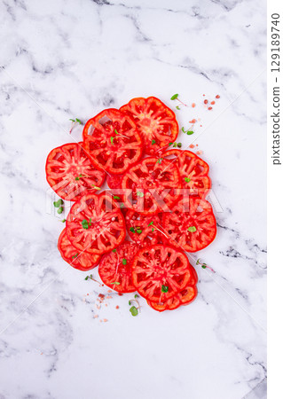 Freshly sliced ripe tomatoes arranged on a marble surface with microgreens and sea salt for a culinary presentation 129189740