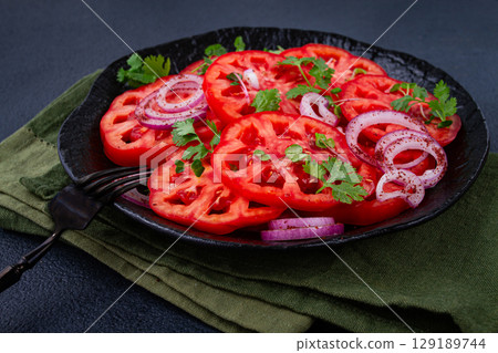 Freshly sliced tomatoes and red onions, garnished with herbs, on a black plate, summer salad, no people 129189744