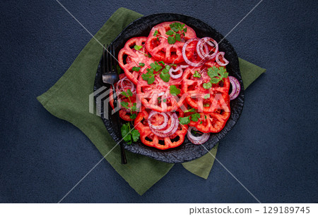 Freshly sliced tomatoes and red onions, garnished with herbs, on a black plate, summer salad, no people 129189745
