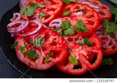 Freshly sliced tomatoes and red onions, garnished with herbs, on a black plate, summer salad, no people 129189747