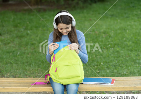Girl listening audiobook with book. Audiobook. Student girl. School education. Student life. School girl listen audiobook in headphones outdoor. Back to school. Education and knowledge. September 1 Girl listening audiobook with book. Audiobook. Student girl. School education. Student life. School girl listen audiobook in headphones outdoor. Back to school. Education and knowledge. September 1 129189868