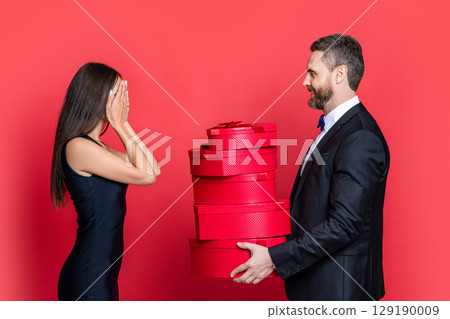 Exchange of gifts. Romantic day together. Love present for anniversary. Valentines day. Couple gives present to the Valentines Day. Man woman hold gift. Elegant couple isolated on red. Dual gifting Exchange of gifts. Romantic day together. Love present for anniversary. Valentines day. Couple gives present to the Valentines Day. Man woman hold gift. Elegant couple isolated on red. Dual gifting 129190009