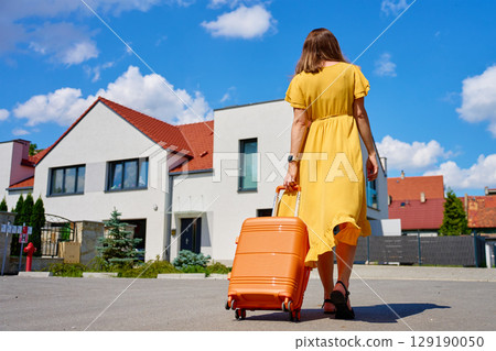 Woman returning home with suitcase after vacation Woman returning home with suitcase after vacation 129190050