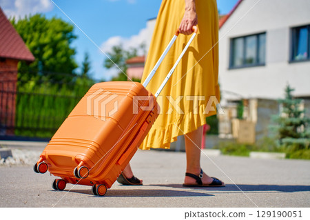 Woman walking with suitcase in suburban neighborhood Woman walking with suitcase in suburban neighborhood 129190051