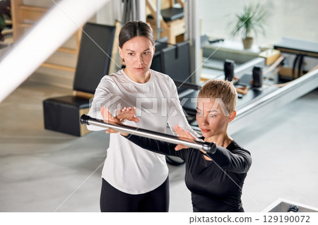 Personal trainer assisting a client with an exercise at a fitness studio Personal trainer assisting a client with an exercise at a fitness studio 129190072
