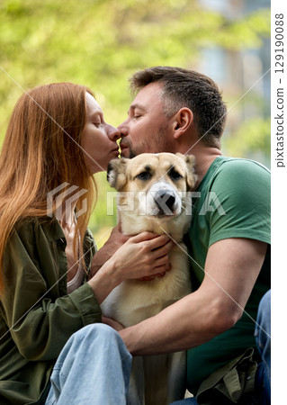 Couple sharing a moment with their dog outdoors in a loving embrace 129190088