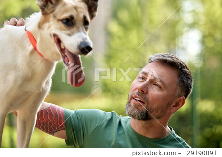 Smiling man bonding with a happy dog outdoors on a sunny day 129190091