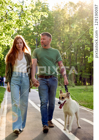 Couple walking their dog on a sunny summer day in a green park 129190097