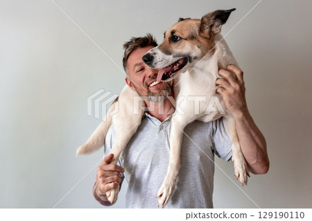 Man joyfully interacts with a dog perched on his shoulders indoors Man joyfully interacts with a dog perched on his shoulders indoors 129190110