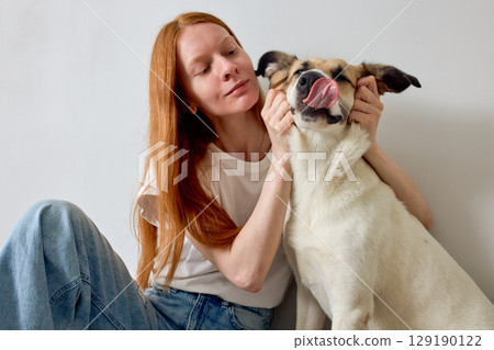 Woman with Long Red Hair Playing with a Happy Dog Indoors 129190122