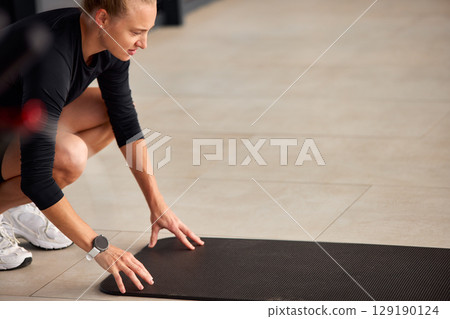 Woman Preparing Yoga Mat for Exercise in Modern Open Indoor Space 129190124