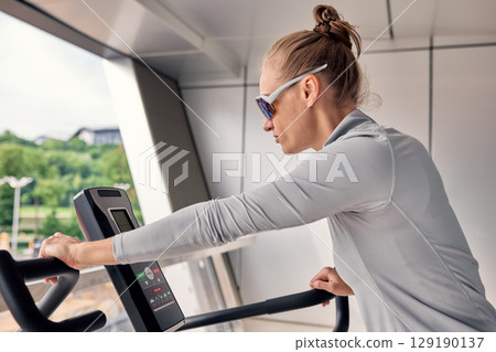 Woman exercising on a treadmill indoors wearing sunglasses and sportswear 129190137