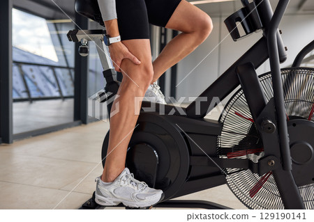 Person experiencing leg discomfort while exercising on a stationary fitness bike 129190141