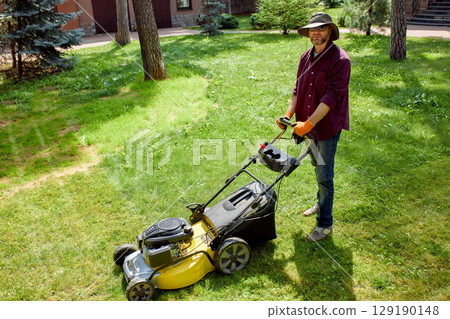 Man in backyard mowing lawn with yellow push mower on a sunny day 129190148