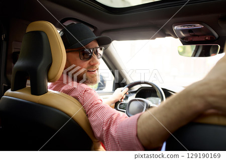 Smiling driver wearing a cap enjoying a sunny day inside a modern vehicle Smiling driver wearing a cap enjoying a sunny day inside a modern vehicle 129190169